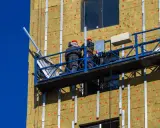 Trabajadores en plataforma instalan aislamiento térmico exterior en edificio.