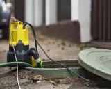 Bomba de agua funciona pero no sube agua. La bomba amarilla y negra está sumergida en una alcantarilla abierta, conectada a una manguera verde.