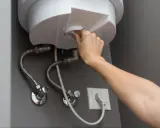 Mano girando el dial para cerrar la llave de paso del termo eléctrico.