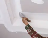 Mano con espátula aplica masilla para reparar techo escayola, dejando un acabado liso y perfecto.