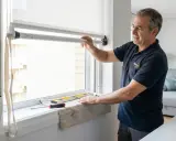 Instalador ajustando uno de los tipos de persianas enrollables. Herramientas y nivel en el alféizar.