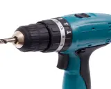 Taladro percutor inalámbrico de color turquesa con broca metálica. El simbolo taladro percutor se ve en su selector de torque.