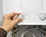 Mano ajustando el dial de temperatura de un termo eléctrico. El agua no sale del termo eléctrico, quizás por la configuración.