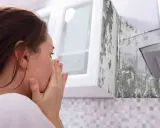 Mujer con las manos en la cara, asqueada por el moho en la pared de la cocina.