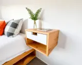 Mesita de noche flotante de madera clara y blanca, ideal para quienes buscan ideas de como hacer una mesita de noche moderna y funcional.