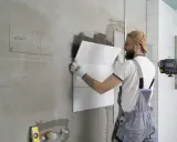 Obrero coloca baldosas en pared, usando nivel láser para asegurar un acabado perfecto. El proceso de instalación de aislante paredes interiores avanza.