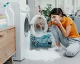 Mujer asustada por espuma saliendo de lavadora. Necesita desatascar desague lavadora para solucionar el problema.