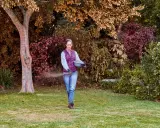 Mujer esparciendo abono en el césped, cuidando su jardín. Es el momento ideal para saber cuándo abonar el césped y asegurar su salud.