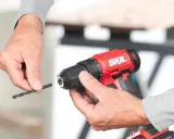 Man insertando una broca en un taladro inalámbrico rojo de la marca SKIL.
