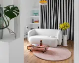 Sofá blanco texturizado, mesa de centro rosa, alfombra redonda y plantas, ideal para una reforma de piso pequeño.