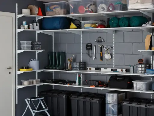 Estanterías metálicas con cajas, herramientas, botas de agua y otros objetos, ideales para saber como organizar un trastero de forma eficiente.