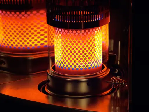 Estufa de parafina encendida, con llama naranja y azul visible a través de perforaciones. Pros y contras de su uso.