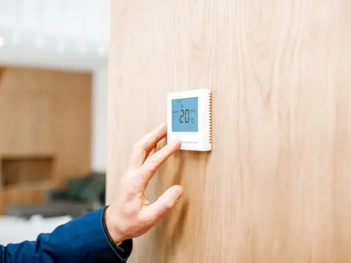 Mano ajustando un termostato digital, parte de los sistemas de calefacción, mostrando 20°C en una pared de madera.