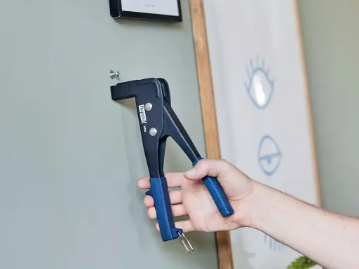 Herramienta para colgar en pladur. Un tornillo se fija a la pared con una remachadora.