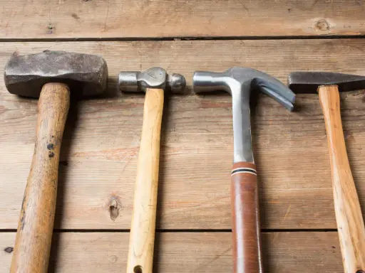 Cuatro martillos de diferentes clases: uno de orejas, uno de bola, uno de carpintero y uno de ebanista, sobre una superficie de madera.