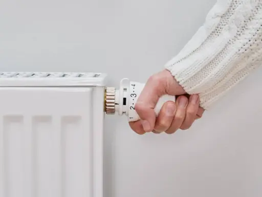 Mano ajustando el termostato de un radiador blanco, pero el radiador no calienta.