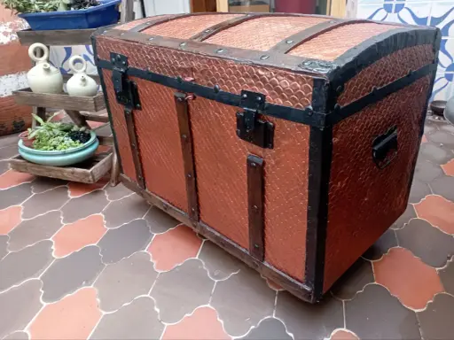 Un baúl antiguo restaurado, con detalles metálicos y acabado en cobre texturizado, listo para guardar tesoros.