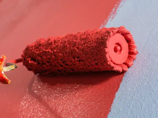Rodillo de pintura roja creando burbujas al aplicarla sobre pared azul.