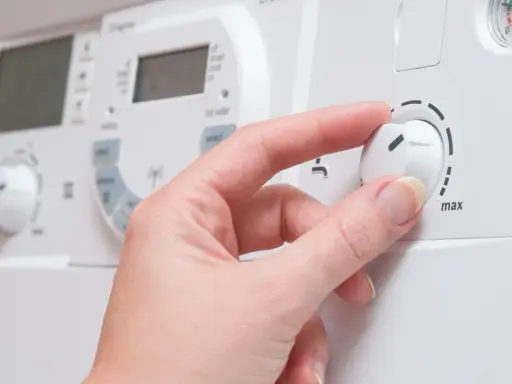 Mano ajustando el dial de una caldera de gas para cambiar la temperatura.