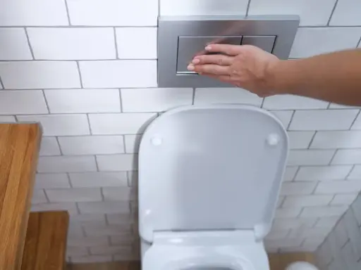 Mano presionando el botón de descarga de una cisterna empotrada, un ejemplo de los modernos tipos de cisternas wc.