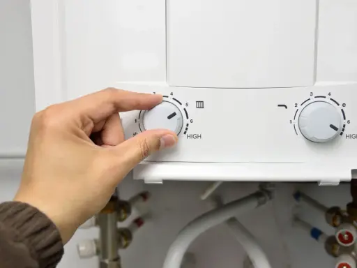 Mano ajustando el dial de temperatura de un termo eléctrico. El agua no sale del termo eléctrico, quizás por la configuración.