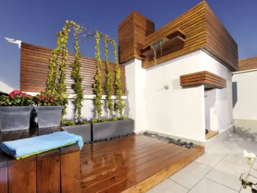 Jardineras de exterior con flores rojas y enredaderas. Un espacio moderno con ducha y terraza de madera.