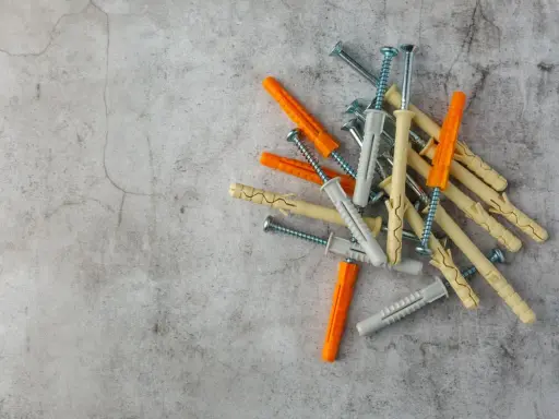 Montón de tacos de pared de varios colores (naranja, gris, beige) con tornillos, listos para fijar cualquier cosa.