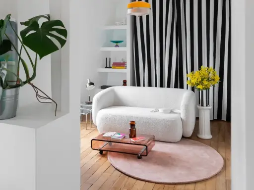 Sofá blanco texturizado, mesa de centro rosa, alfombra redonda y plantas, ideal para una reforma de piso pequeño.