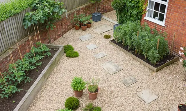 Un huerto urbano en terraza con tomates y habas en bancales de madera, senderos de grava y plantas en macetas.