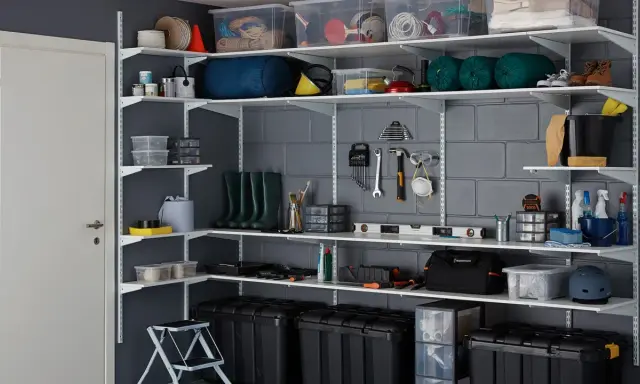 Estanterías metálicas con cajas, herramientas, botas de agua y otros objetos, ideales para saber como organizar un trastero de forma eficiente.