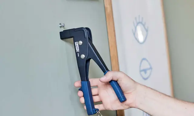 Herramienta para colgar en pladur. Un tornillo se fija a la pared con una remachadora.