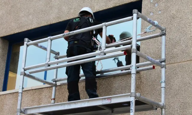 Trabajador en andamio modular, uno de los tipos de andamios, limpiando una ventana.