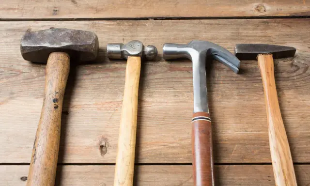 Cuatro martillos de diferentes clases: uno de orejas, uno de bola, uno de carpintero y uno de ebanista, sobre una superficie de madera.