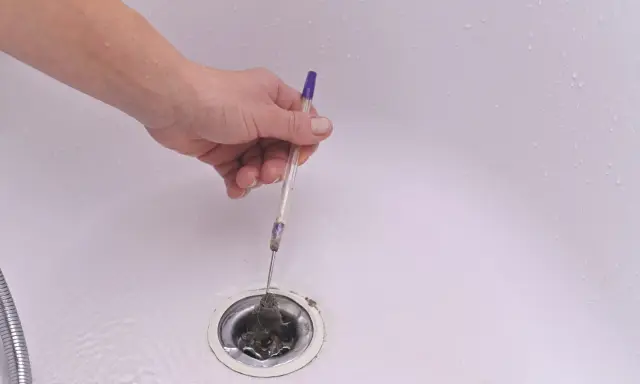 Mano usando un bolígrafo para desatascar desague ducha lleno de pelo.