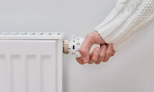 Mano ajustando el termostato de un radiador blanco, pero el radiador no calienta.