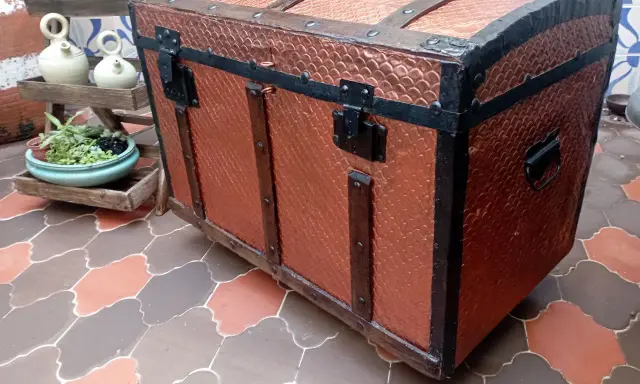 Un baúl antiguo restaurado, con detalles metálicos y acabado en cobre texturizado, listo para guardar tesoros.