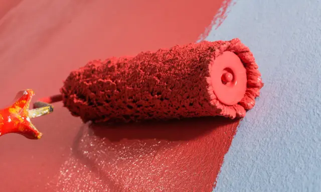 Rodillo de pintura roja creando burbujas al aplicarla sobre pared azul.