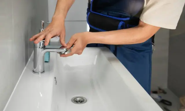 Man con mono azul trabajando en el baño, ajustando un grifo nuevo para cambiar grifo lavabo.