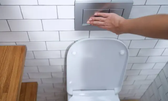 Mano presionando el botón de descarga de una cisterna empotrada, un ejemplo de los modernos tipos de cisternas wc.