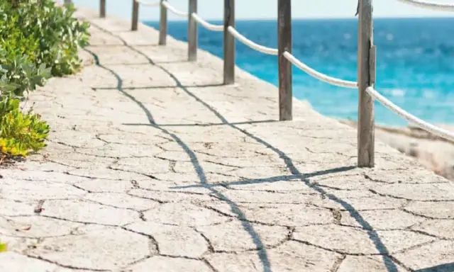 Camino de piedra con barandilla y mar azul. Un ejemplo de cómo hacer hormigón impreso para exteriores.