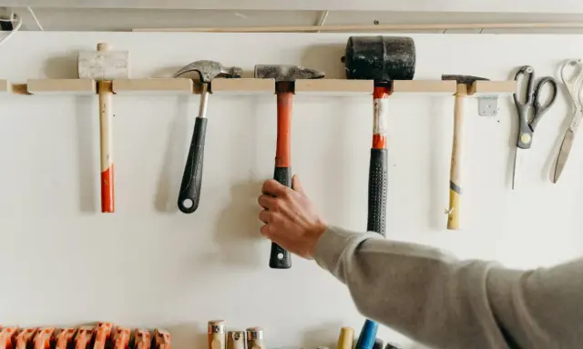Variedad de tipos de herramientas manuales, incluyendo martillos, mazos y tijeras, colgadas en una pared.