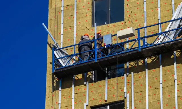 Trabajadores en plataforma instalan aislamiento térmico exterior en edificio.