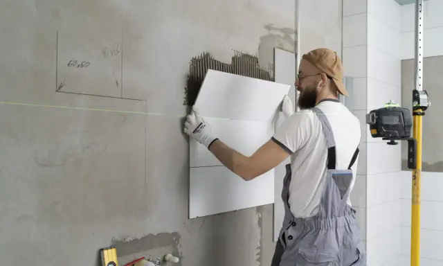 Obrero coloca baldosas en pared, usando nivel láser para asegurar un acabado perfecto. El proceso de instalación de aislante paredes interiores avanza.