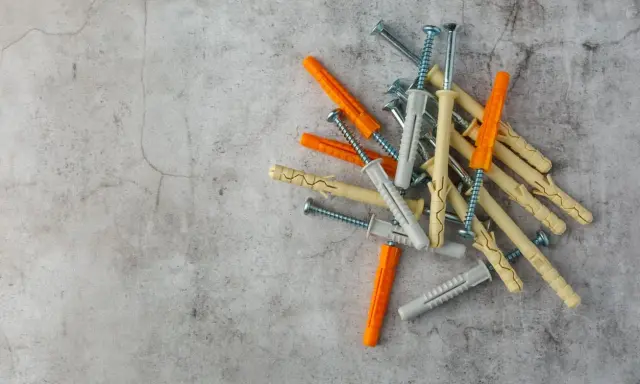 Montón de tacos de pared de varios colores (naranja, gris, beige) con tornillos, listos para fijar cualquier cosa.