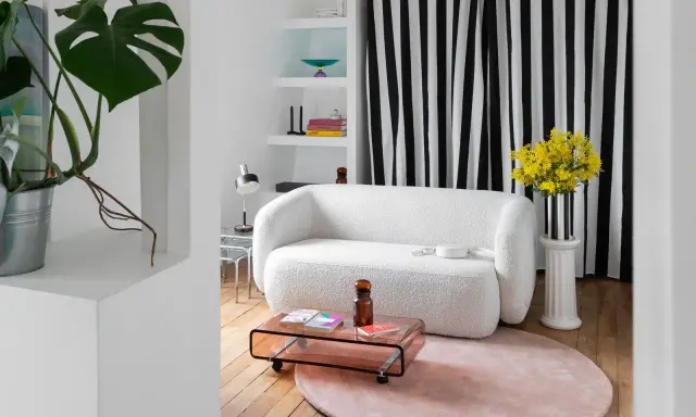 Sofá blanco texturizado, mesa de centro rosa, alfombra redonda y plantas, ideal para una reforma de piso pequeño.