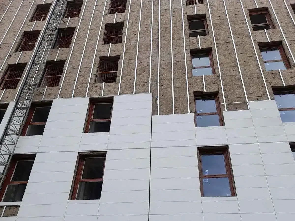 Fachada en construcción con aislamiento térmico exterior y ventanas de madera.