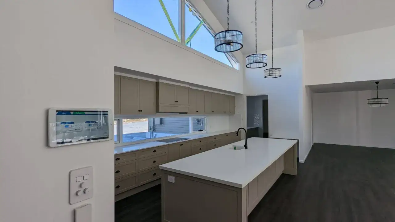 Panel táctil controla la climatización por conductos en una cocina moderna con isla central y gabinetes color arena.