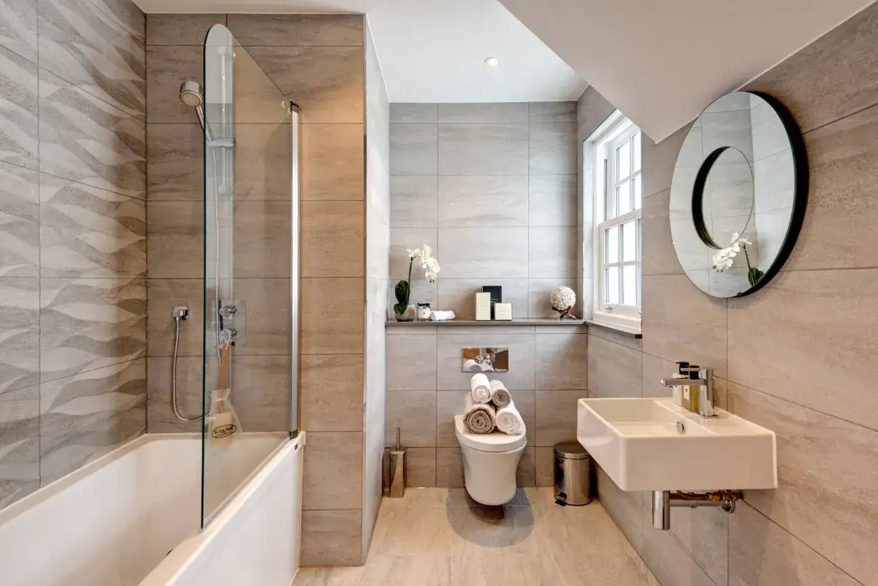 Ba&ntilde;o moderno con ducha, ba&ntilde;era y lavabo. El inodoro, con varios tipos de cisternas wc visibles, est&aacute; decorado con toallas.