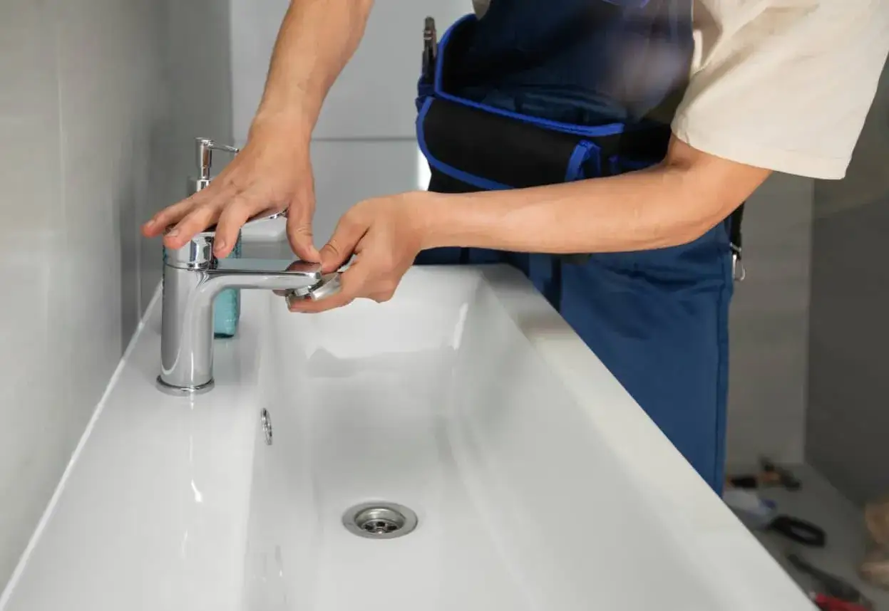 Man con mono azul ajustando un grifo nuevo en un lavabo blanco.