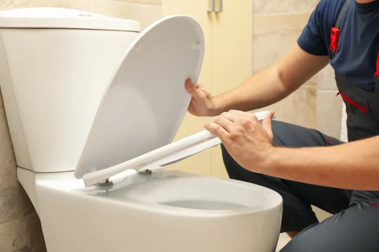 Man installing a toilet seat. This inodoro has a vertical or horizontal outlet, ensuring compatibility with various plumbing setups.
